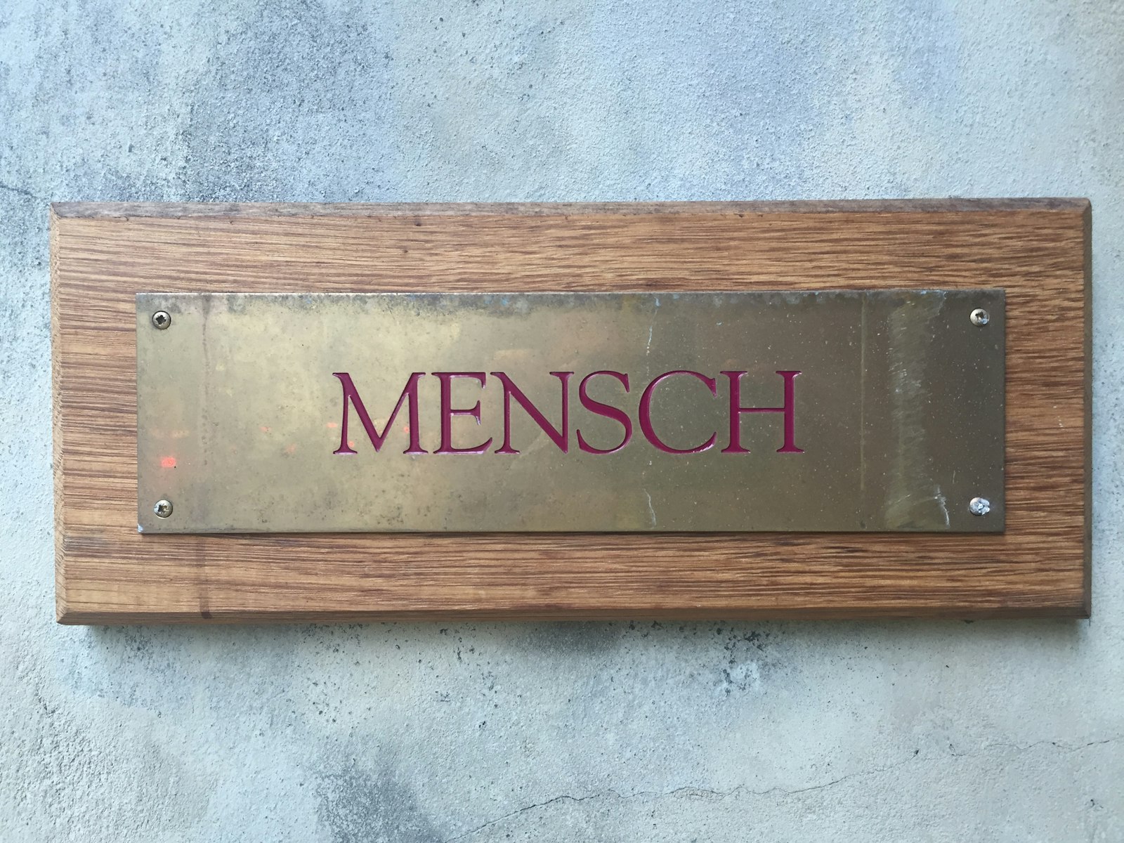 Placa de metal dorado con letras grabadas en rojo, montada sobre una base de madera.